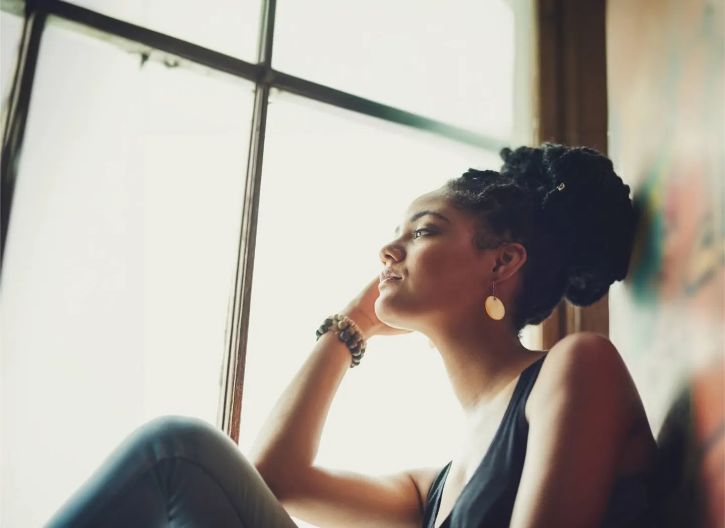 A young woman looking out a bright window, lost in thought