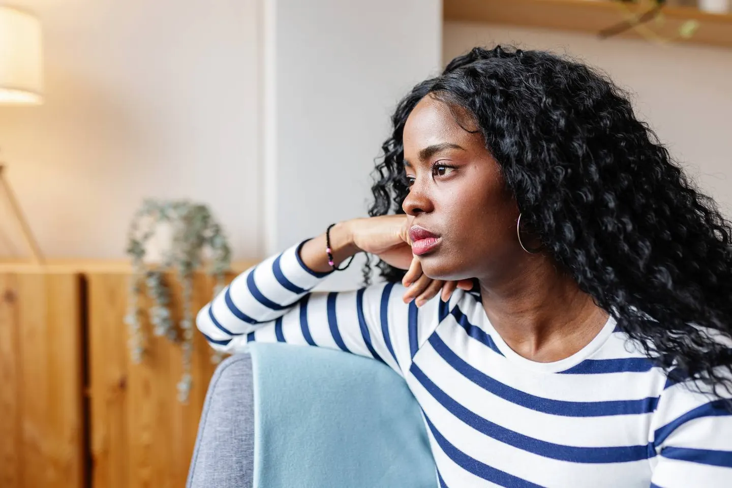 A young woman in a striped shirt resting her chin on her hand, gazing thoughtfully