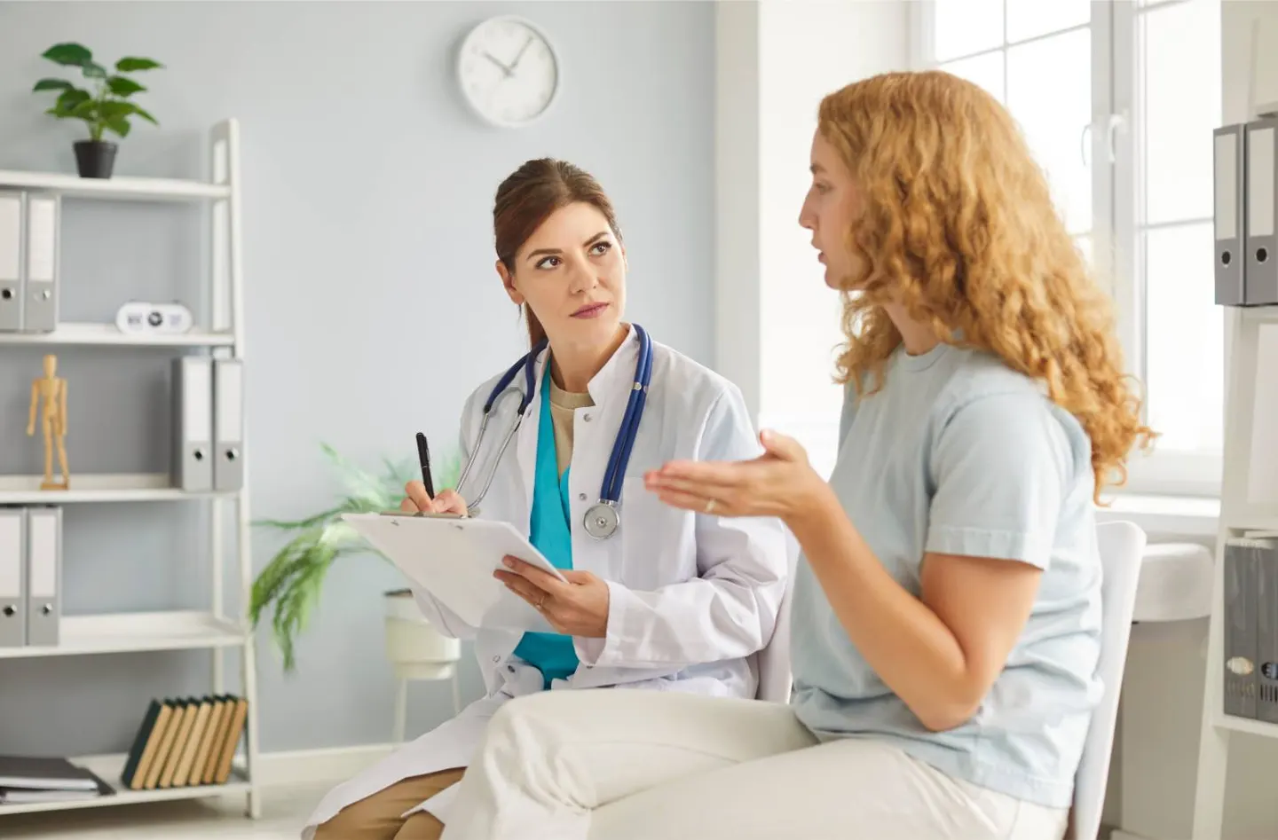 A clinician in a white coat talking with a young woman in an exam room